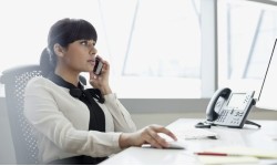 A photograph of a lady on the phone sitting at a computer