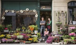 A photograph of a flower shop with 3 people standing in the doorway