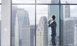 A photograph of a man on the phone looking out of a large office window