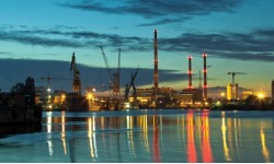 A photograph of night skyline across water with cranes in the background