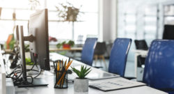 A photograph of an office desk with 3 blue chairs and a computer screen